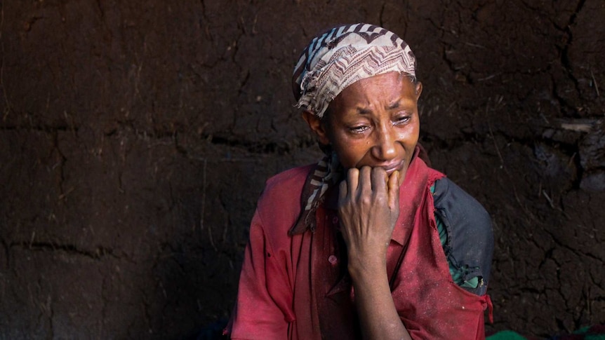Ethiopian woman Almaz Tilhun wears a patterned head scarf and cries with her hand at her mouth.