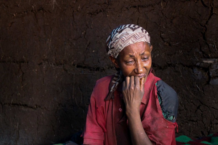 Ethiopian woman Almaz Tilhun wears a patterned head scarf and cries with her hand at her mouth.