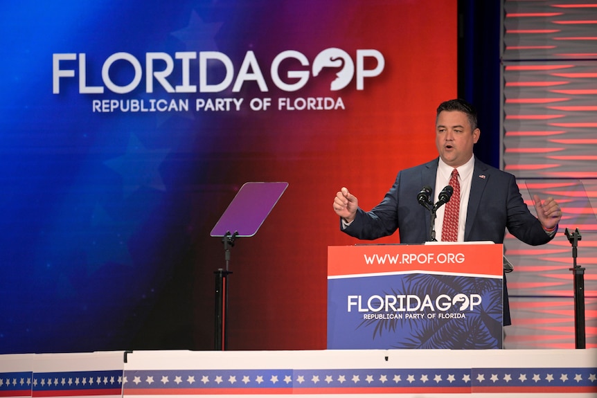 Christian Ziegler stands at a podium. A secreen behind him says 'Florida GOP Republican Party of Florida'