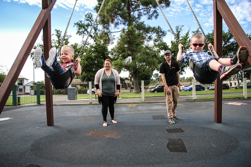 The Goudie family at the park with the two brothers on swings.