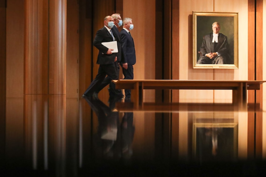 Josh Frydenberg, Scott Morrison and Michael McCormack walk through parliament in facemasks, their images reflected on the floor