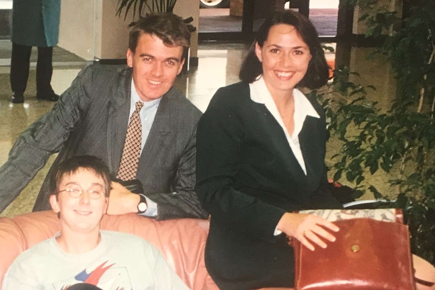 Rowland standing behind couch with Ainsworth and Millar sitting in hotel lobby.