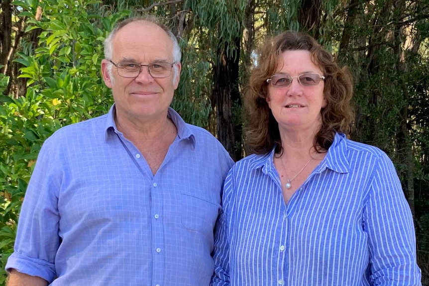 A man and woman stand side by side in the Australian bush.