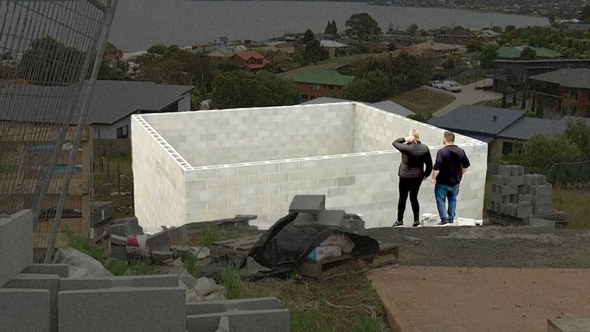 A couple stand next to an unfinished home.