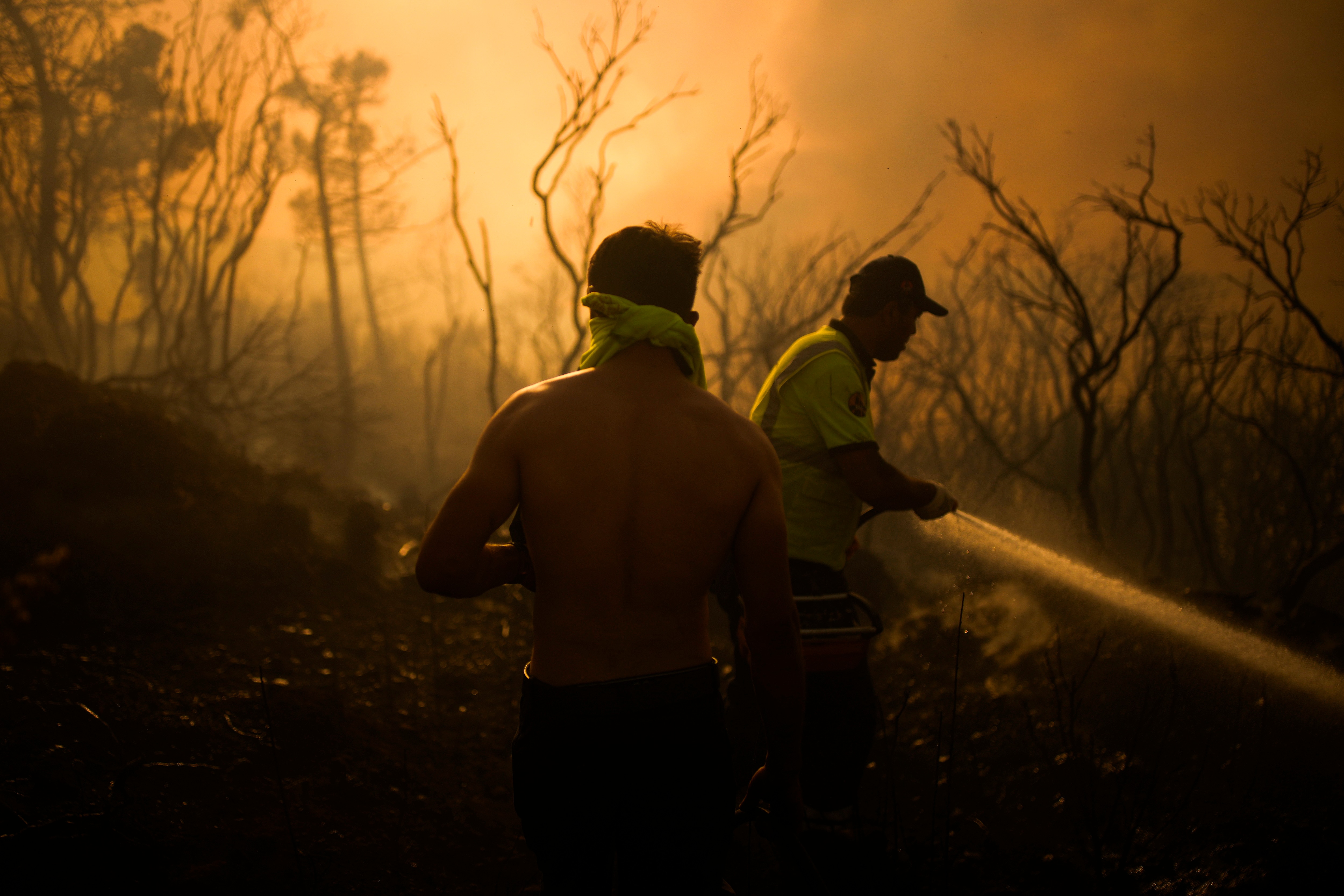 Two man, one shirtless, surrounded by orange glow of fire 