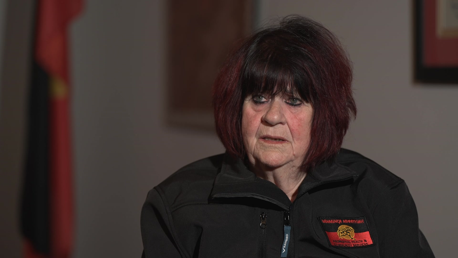 An Aboriginal woman with dark hair tipped with red speaking seriously.