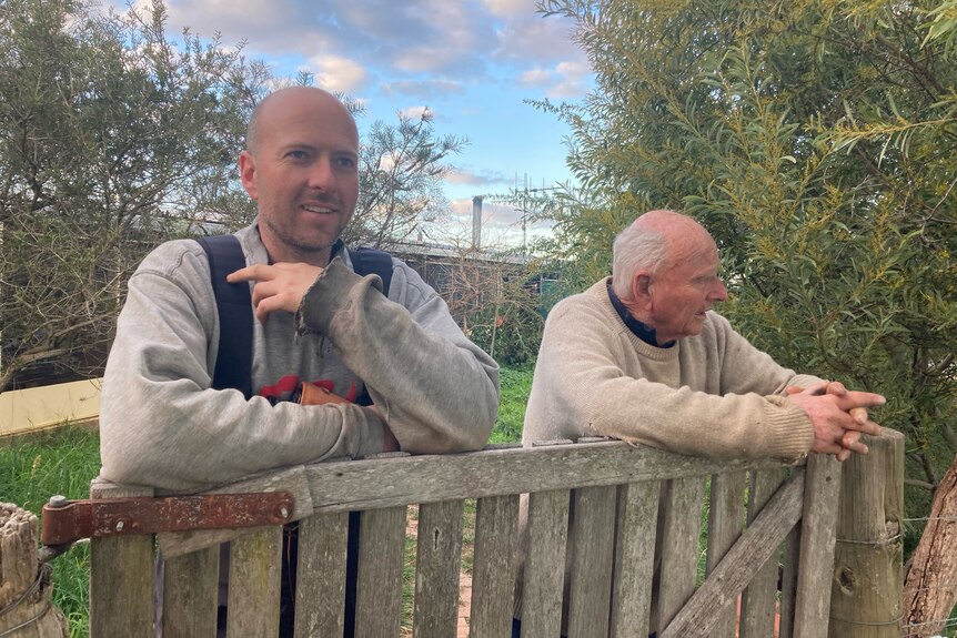 Two men learning on a fence. 