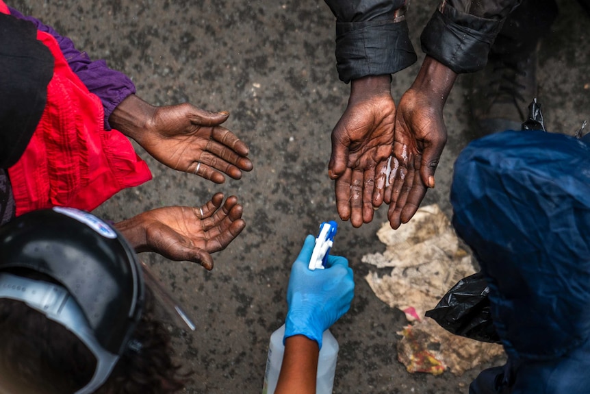 Two pairs of hands are held out with a person spraying hand sanitiser. Photo shot from above looking down.