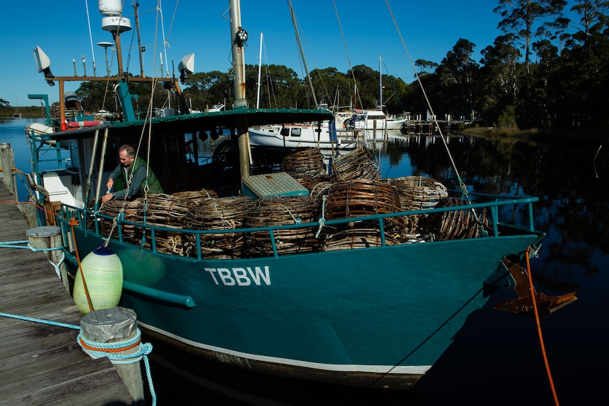 A green-coloured crayfish boat with pots on the front.