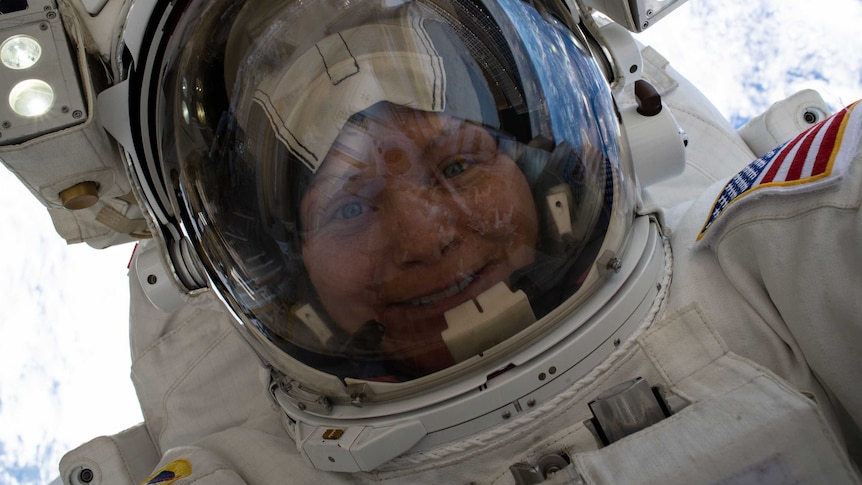 An astronaut smiles as they take a selfie during a spacewalk miles above the Earth's surface, with Earth in the background