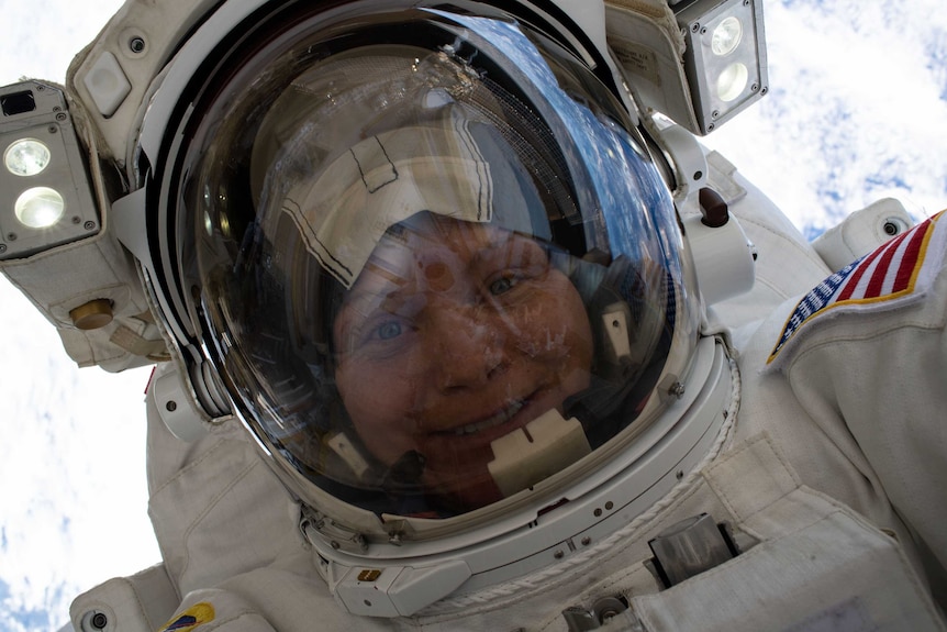 An astronaut smiles as they take a selfie during a spacewalk miles above the Earth's surface, with Earth in the background