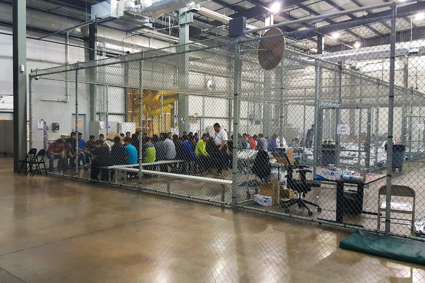 Kids sit on benches inside a cage.