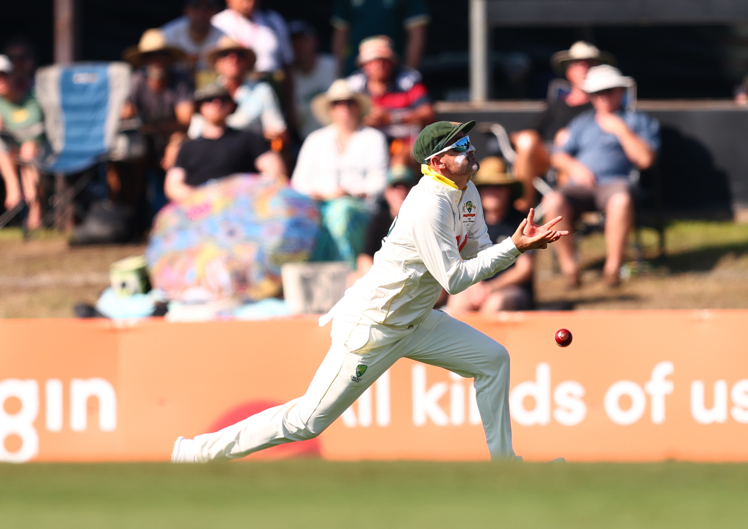 A cricket player in white and sunglasses drops a catch in afternoon sun