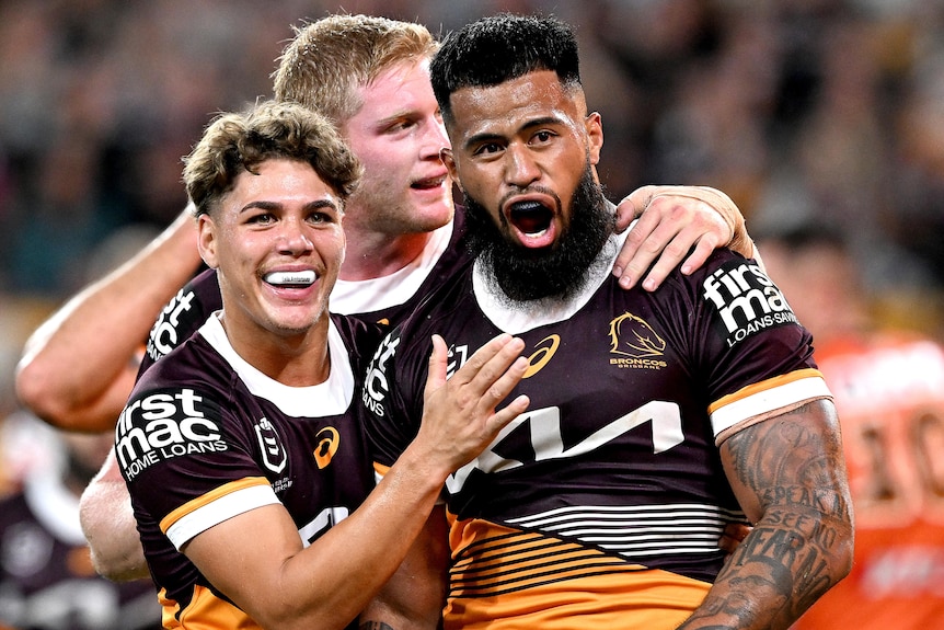 Three Brisbane Broncos NRL players embrace as they celebrate a try.