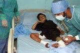 Doctors treat a boy on a hospital bed with bandages and wounds on his legs.