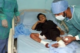 Doctors treat a boy on a hospital bed with bandages and wounds on his legs.