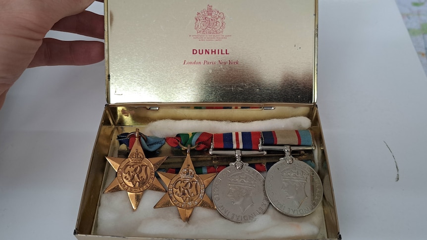 Four medals are displayed inside a gold tin on a white cotton inlay.