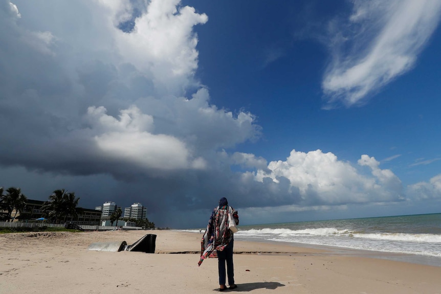 Man sands on beach as huge grey storm clouds gather