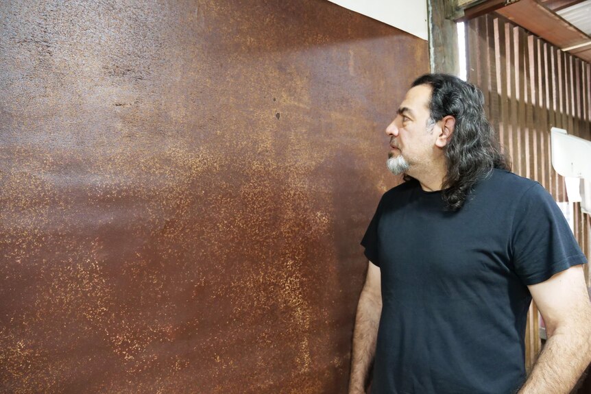 A man looks at a painting of brown splotches