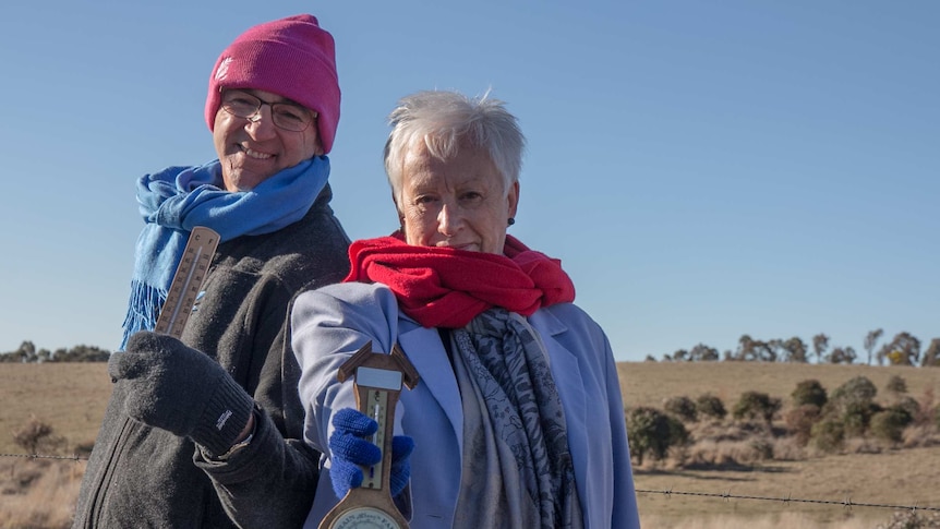 A man and woman in beanies, gloves and scarves holding a thermometer and barometer