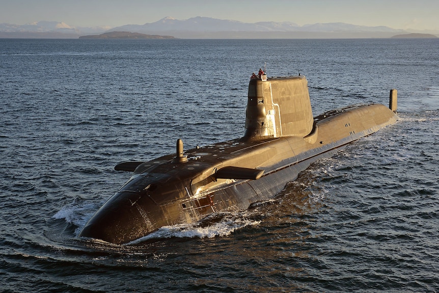 A submarine at the surface with morning sun on its right flank, the ocean stretches behind it