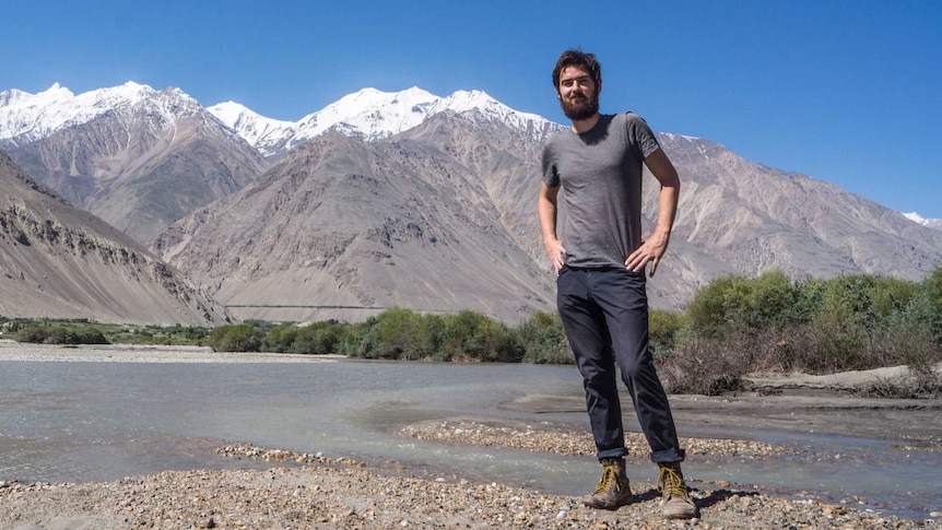 A youngish guy standing in front of a snow-capped mountain smiling