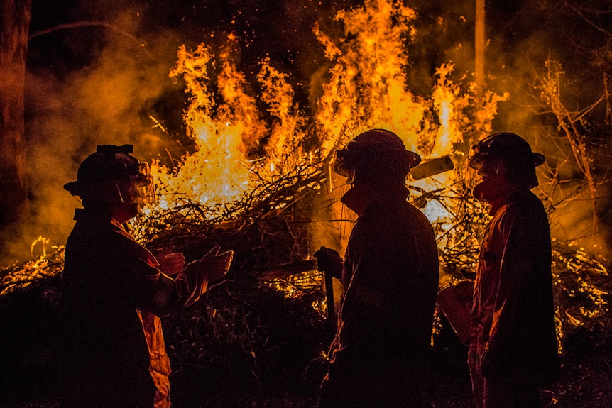 Three firefighters watch over a controlled burn.