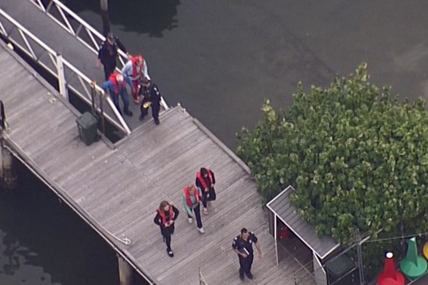 Police walk with people wearing life jackets on a boat ramp near the water