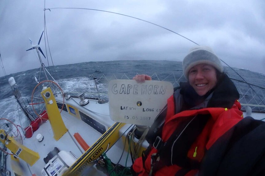 A woman on a yacht at sea holding a sign saying Cape Horn.