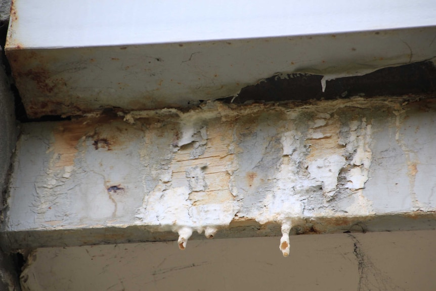 A rotting, rusted wooden beam with paint dripping off.