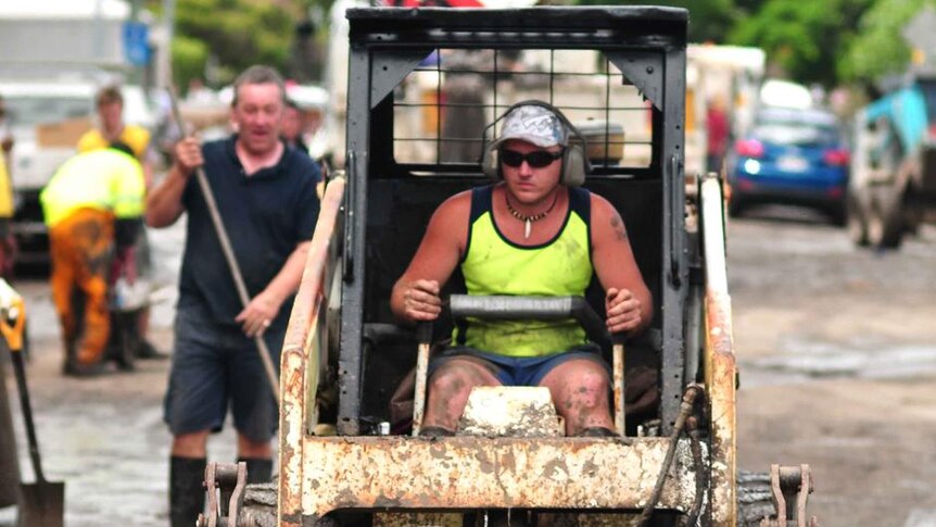 A man in a bobcat helps clear mud and debris from a street in Fairfield, Brisbane on January 15, 2011.