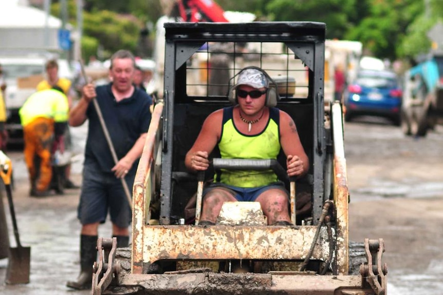 A man in a bobcat helps clear mud and debris from a street in Fairfield, Brisbane on January 15, 2011.
