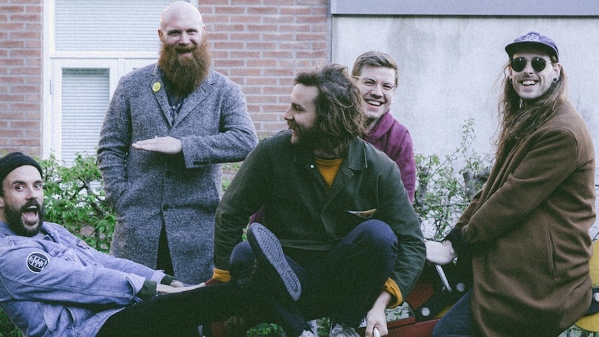 British punk band IDLES sit, smiling, outdoors