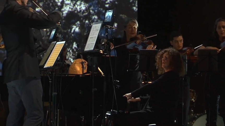 A pianist performing on stage with an orchestra.