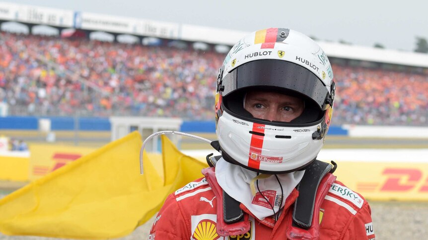 Sebastian Vettel walks away from the gravel trap wearing his helmet with banks of spectators behind