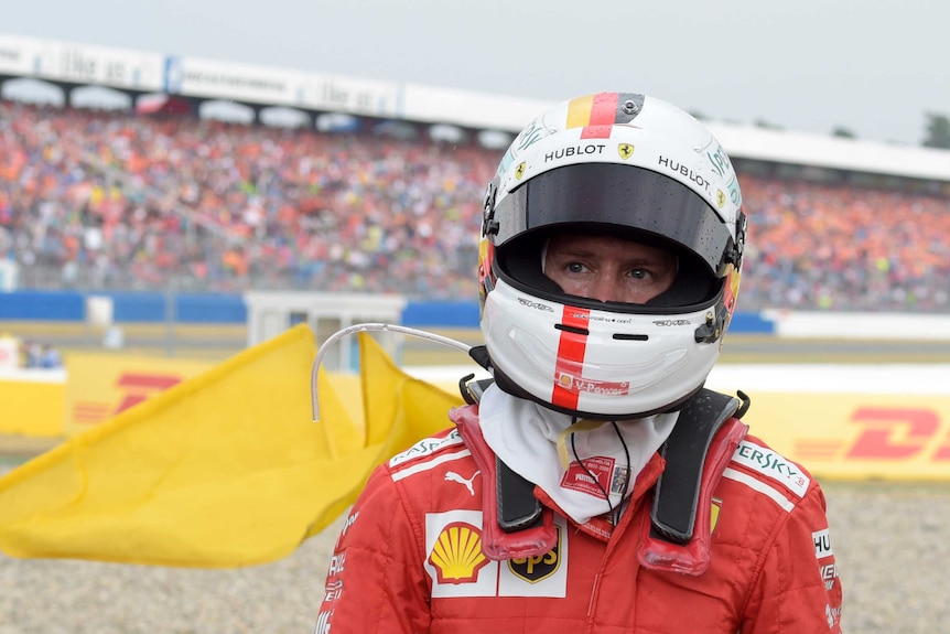 Sebastian Vettel walks away from the gravel trap wearing his helmet with banks of spectators behind