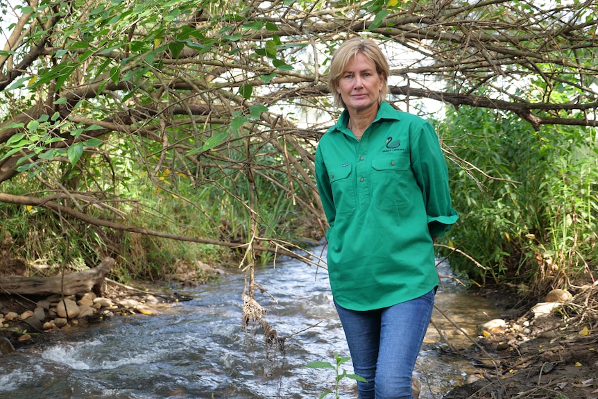 A woman in a green shirt stands by a creek