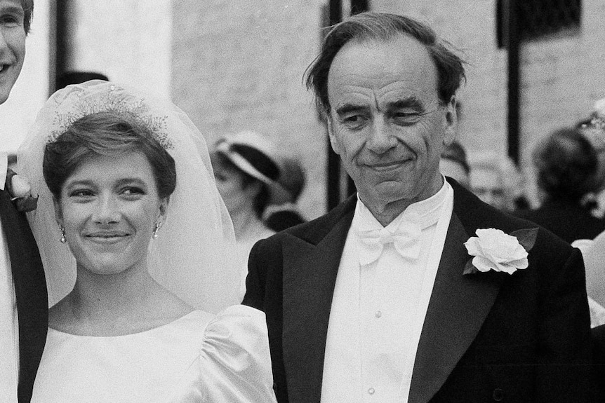 A black and white photo of Rupert Murdoch in a tuxedo standing next to a smiling bride 