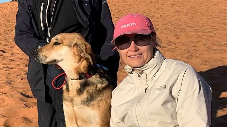 A dog sits on a sand dune between a man and a woman.