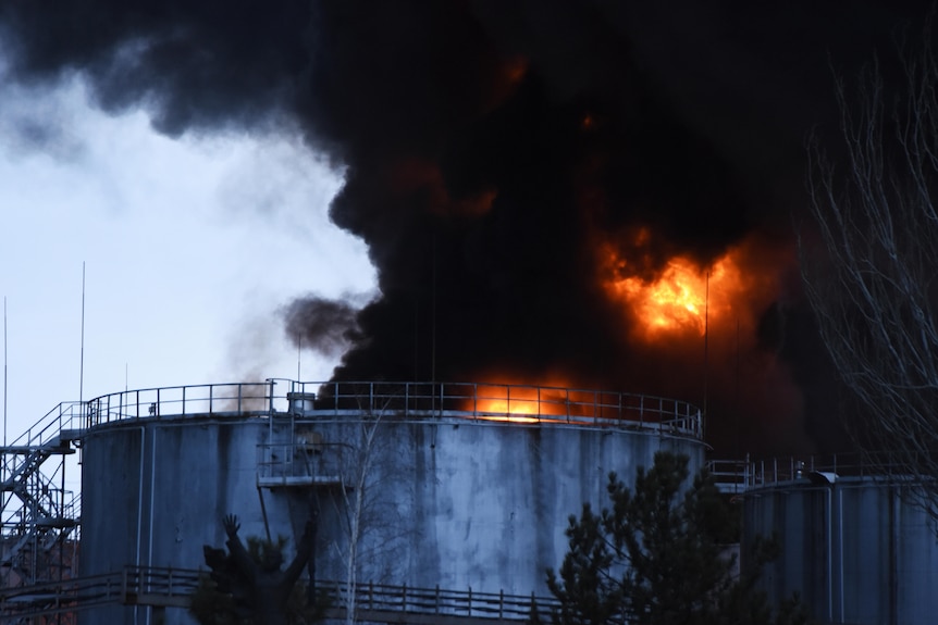 Smoke rises from flames from a large tank.