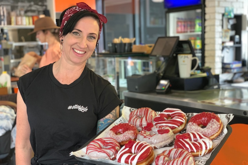 A woman holds a tray of maroon-coloured doughnuts in honour of the Queensland team ahead of State of Origin. 
