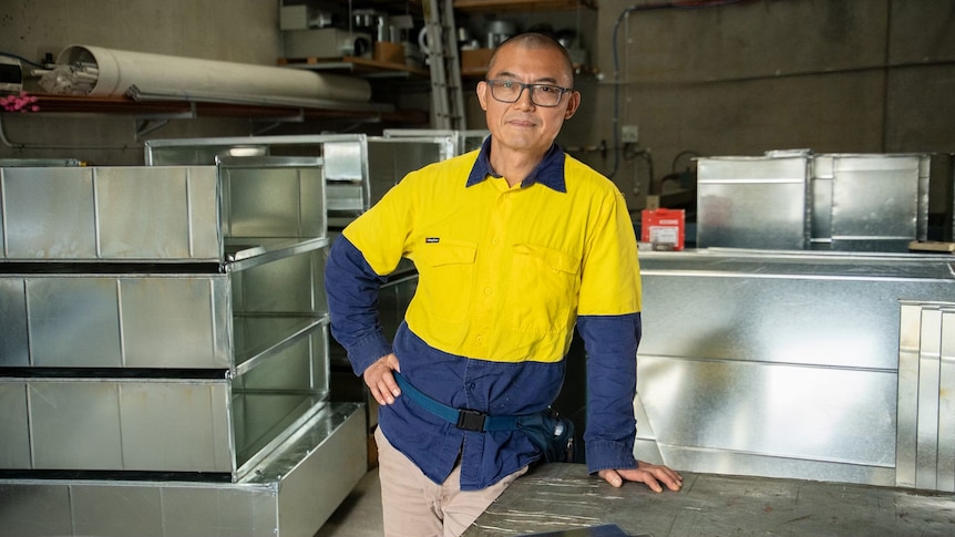 Yaning learning on a workbench with a serious expression, wearing a high-vis shirt.