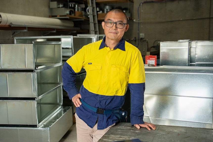 Yaning learning on a workbench with a serious expression, wearing a high-vis shirt.