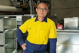 Yaning learning on a workbench with a serious expression, wearing a high-vis shirt.