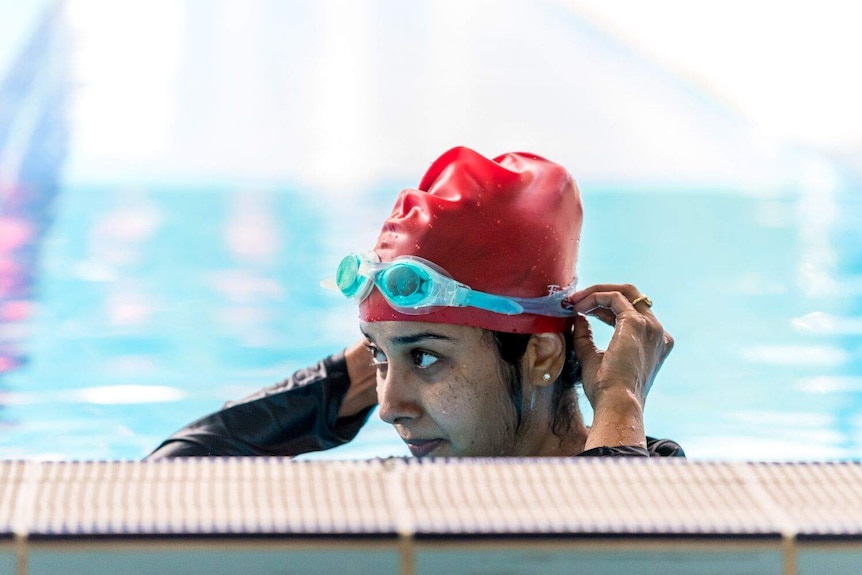 A woman stands in a pool adjusting her swimming cap.