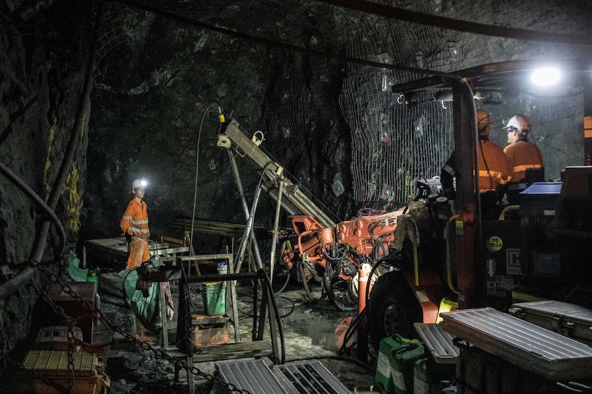 Workers wearing high-vis clothing in an underground mine drilling for gold.