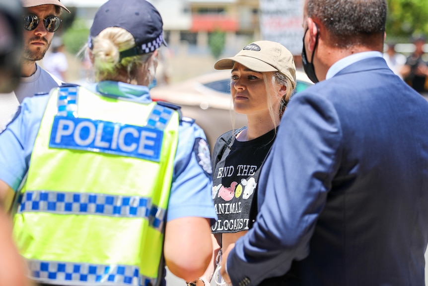 A woman in a black shirt and beige hat is spoken to by police