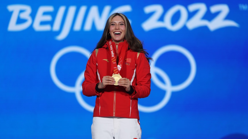 A Chinese female athlete stands with her gold medal at a ceremony at the Beijing Winter Olympics.