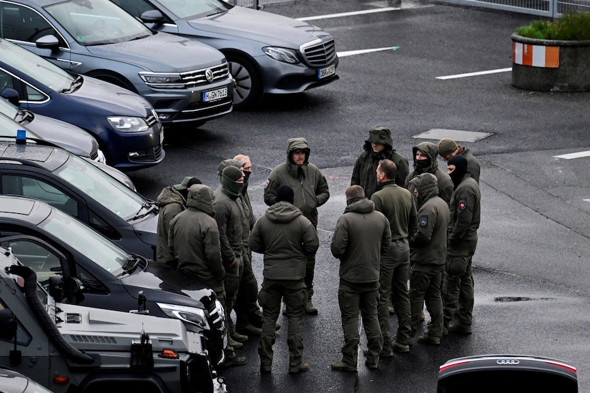 An image of police officers dressed in army green attire circled in front of police cars.