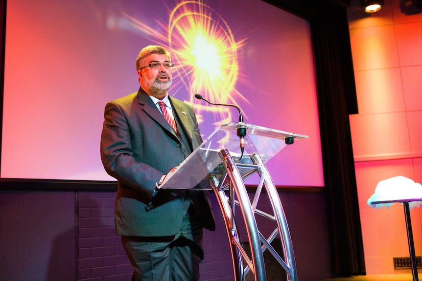 Former science minister Senator Kim Carr standing behind a podium  launching the Hello From Earth campaign at Questacon